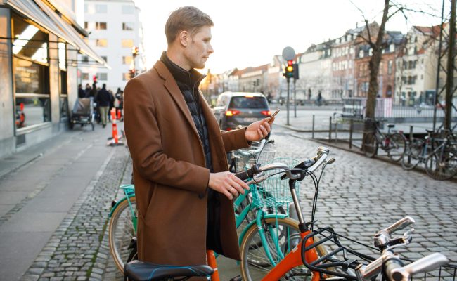 Young man unlocks bicycle with his mobile phone. Electric bicycle new way city mobility. Green transportation. Sustainable climate neutral cities goals. Ecology mobility sustainability transportation